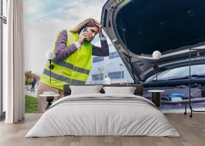 Young Caucasian woman, talking on her cell phone while her car is broken down on the road Wall mural