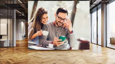 Young cheerful man and woman dating and spending time together in cafe, using phone. Wall mural