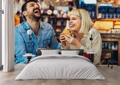 Young couple in love having fun spending leisure time together at restaurant, eating burgers and drinking beer Wall mural