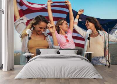 Young female friends carrying american flag on the beach Wall mural