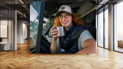 Young ginger woman driving long vehicle and drinking coffee so she could get some energy. Wall mural