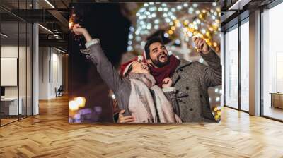 Young loving couple burning sparklers by holiday illumination on new years eve. Wall mural