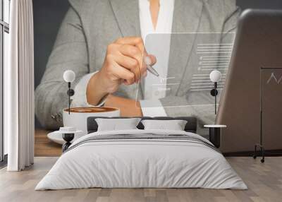 A businesswoman in a suit uses a pen to sign electronic documents on a virtual screen while sitting at the table in the office Wall mural