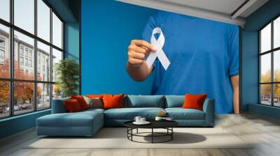 A female hand is holding a white ribbon on a blue background Wall mural