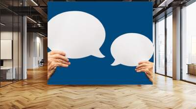 Close-up of a senior woman's hands holding a blank white speech bubble against a blue background. Wall mural