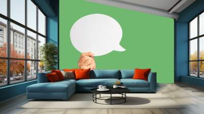 Close-up of hand holding a green speech bubble against a green background Wall mural