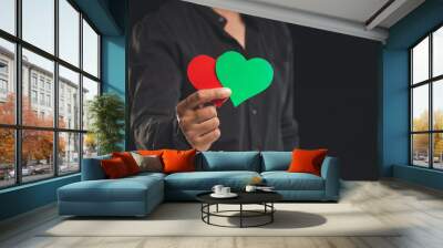 Close-up of hand holding green and red hearts shape symbol while standing on a black background Wall mural