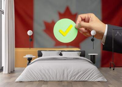 Hand holding a check mark symbol overhead the voting box at place election with the Canada flag background Wall mural