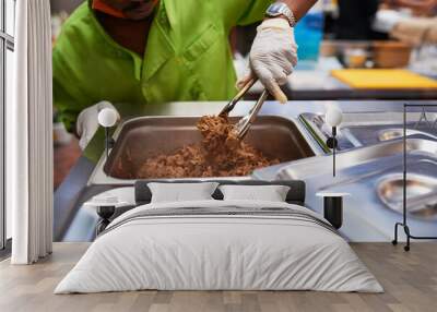 A chef assistant gets a portion of pulled beef with tongs Wall mural