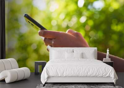 Close up of Black woman's hands using mobile phone, texting in nature leaf bokeh Wall mural