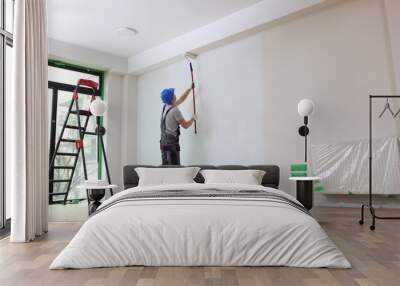 Male painter paints house wall with roller brush. Wall mural