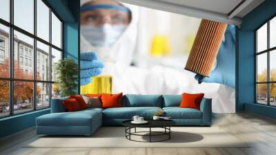 Scientist in protective suit holds car filter cartridge in laboratory and oil Wall mural