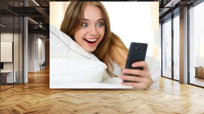 Young beautiful blonde woman lying in bed and holding cellphone Wall mural