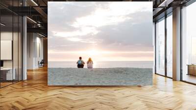 Two People Watching the Beautiful and Serene Sun Set Over the Ocean Horizon While Sitting in the Sand at the Tropical Beach Wall mural