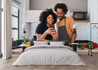 Afro couple cooking together and using phone at home. Wall mural