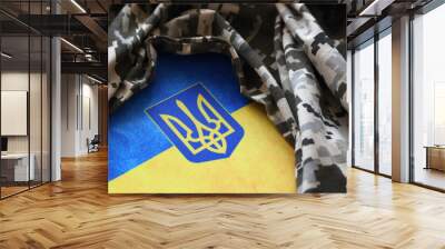 Ukrainian flag and coat of arms with fabric with texture of pixeled camouflage. Cloth with camo pattern in grey, brown and green pixel shapes with Ukrainian trident sign Wall mural