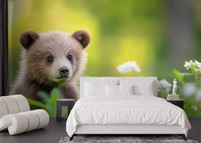 A baby bear is standing in a field of flowers. The bear is looking at the camera with a curious expression. The scene is peaceful and serene, with the baby bear surrounded by nature Wall mural