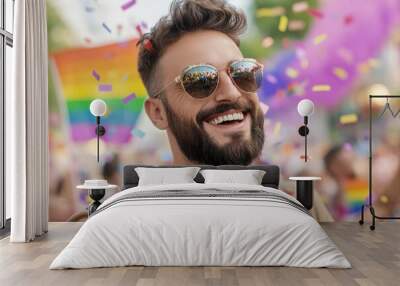 A man with a beard and sunglasses is smiling, surrounded by confetti in the streets of a carnival, wearing a brown shirt, and the background features colorful pride flag Wall mural