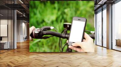 Female hands holding a smartphone while sitting on a mountain bike on a forest road. Concept navigation, summer active sports, technology. Wall mural