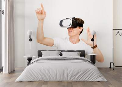 Male using virtual reality headset interacts with augmented things orienting in three dimensional space while sitting on his desk with keyboard and laptop on white background. Wall mural