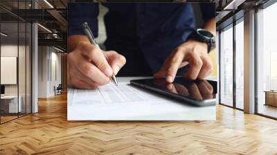 businessman working in the office. he is using touchpad reading an email on tablet and taking notes on the paper with soft-focus and over light in the background Wall mural