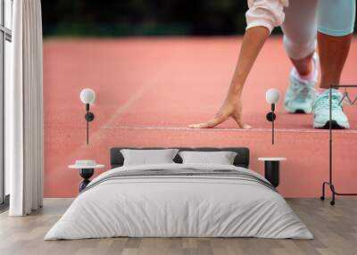 Athlete in starting position on running track, wearing light blue athletic shoes and white leggings, preparation and determination before race Wall mural