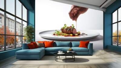 Chef's hand garnishing a beef steak with vegetables on a white plate Wall mural