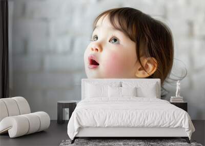 A little girl with brown hair and a pinkish face is looking up at something Wall mural