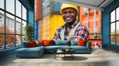 A man in a yellow helmet and orange vest stands in front of a row of shipping containers. Concept of hard work and dedication, as the man is likely a worker in a warehouse or shipping facility Wall mural