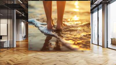 A person's feet are in the ocean water, with the sun setting in the background Wall mural