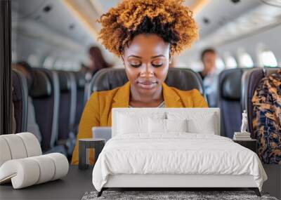 A woman with curly hair is sitting on a plane and using a laptop Wall mural