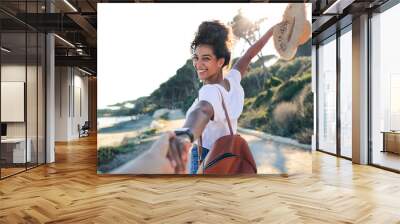 Woman walking on a path by the sea, holding a friend's hand Wall mural