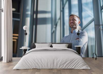 Businessman in casual attire standing with arms crossed near large windows Wall mural