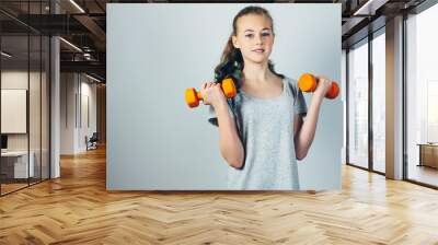 Beautiful caucasian teen girl doing exercises with dumbbells.  Gray studio background, copy space. Fitness and healthy sports lifestyle. Wall mural