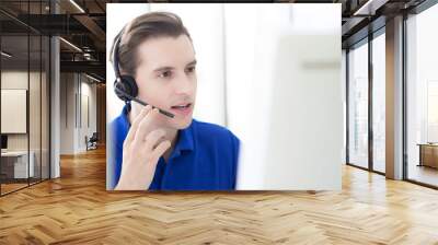 call centre. close up smiling friendly handsome young male blue shirt operator working with headset in front of computer screen. Technical support Customer Service agent in an startup office. Wall mural