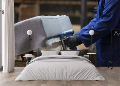 Closeup of a young man in a furniture factory who puts together one part of the sofa with a stapler Wall mural