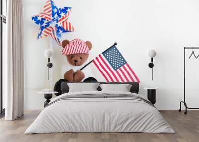 One teddy bear in a red striped hat is sitting and holds the flag of America. Light background, indoors. USA Independence Day Background. Picnic on July 4th. Copy space for text. San Francisco, USA Wall mural