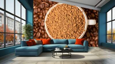 There is a white cup of ground coffee on top of the sprinkled beans. Close-up. Wall mural