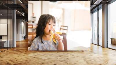 Happy Little girl eating banana.5 years old girl eat banana in restaurant. Wall mural