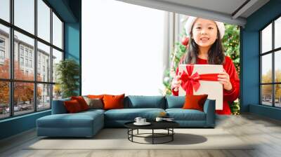 Little asian girl smile and excited and holding red gift box on christmas tree and white background.Child girl holding gift box in Christmas celebration and Happy New year concept. Wall mural