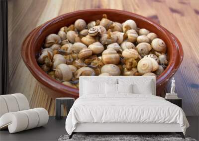 A terracotta bowl with snails in broth, on a wooden table. Spanish tapas highly demanded. Spanish food concept. Wall mural