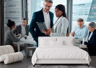 Be smart about your business processes. Shot of two businesspeople using a digital tablet in an office with their colleagues in the background. Wall mural