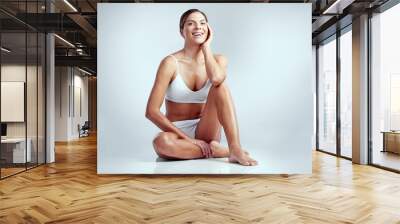 Beauty and confidence. Studio portrait of an attractive young woman sitting on the floor against a grey background. Wall mural