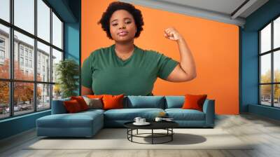 My strength comes from within. Shot of a beautiful young woman flexing while standing against an orange background. Wall mural