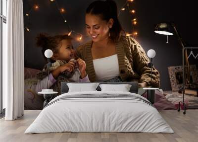 Night, book and learning with mother with daughter in bedroom for storytelling, fantasy and smile. Education, fairytale and love with woman reading to girl in family home for bedtime, happy or relax Wall mural