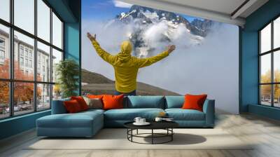 A tourist in a yellow jacket and a knitted hat on the top of high rocks. Sports and active life concept Wall mural