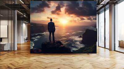 Businessman standing on cliff and watching sunset over ocean. Wall mural