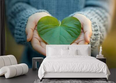 Child holding a heart-shaped green leaf in open palms as a symbol of nature's love Wall mural