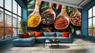 Colorful spices and herbs resting in wooden spoons on black slate Wall mural