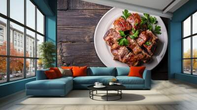 Delicious grilled and sliced pork ribs with parsley on a white plate on a rustic wooden table Wall mural